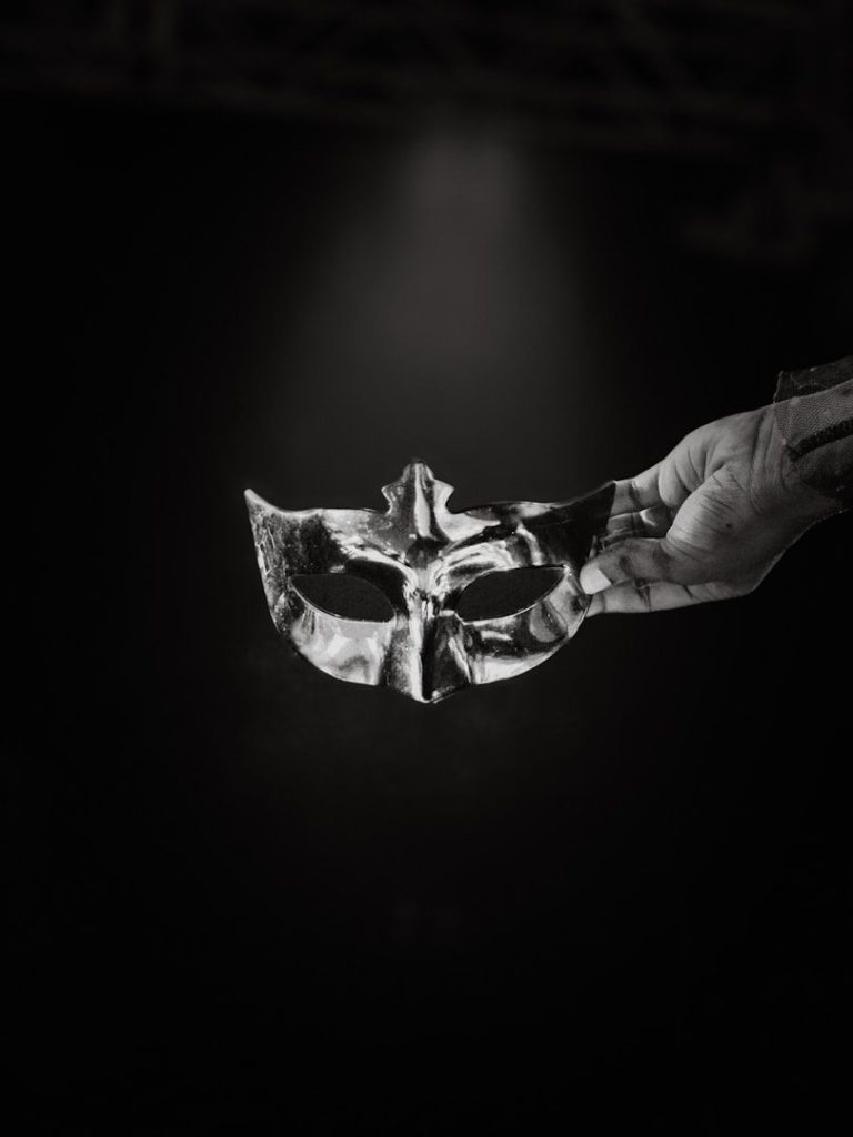 Eine Hand hält eine maskierte Maske vor dunklem Hintergrund.